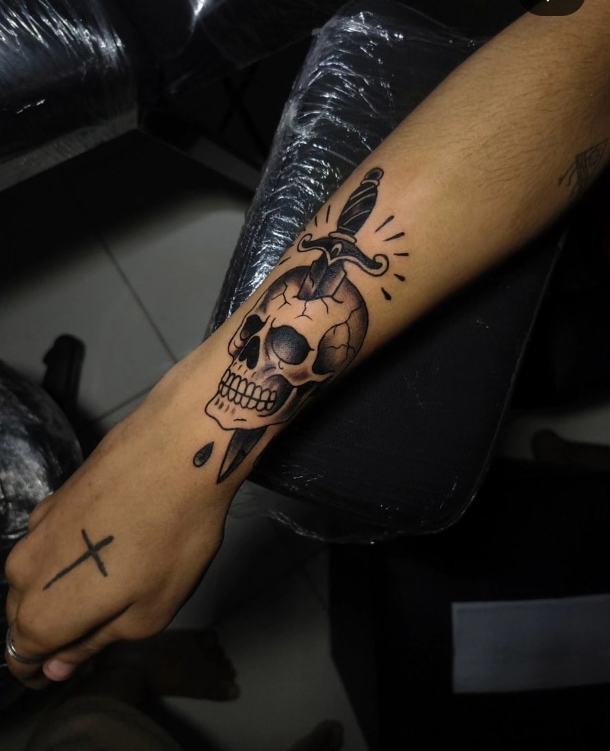 Tatuagem de caveira com adaga no antebraço, estilo blackwork